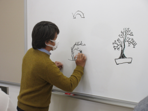 盆栽のイラストをホワイトボードに描き説明する講師
