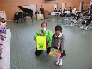 加西安全協会の本岡博文事務局長が新入生にランドセルカバー等を手渡した写真
