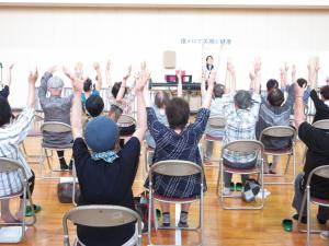 椅子に座って両手を上げる体操をする受講生の写真