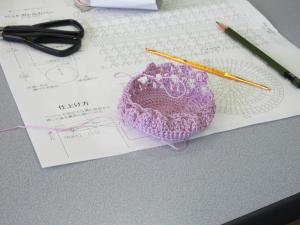 編みあがった底の部分と編み針、編み図の写真