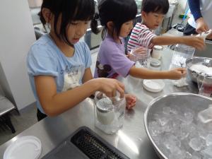 容器にアイスクリームの材料であるグラニュー糖を入れる子供たち（アイスつくり２）