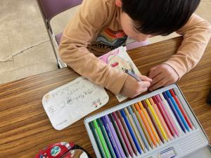 描いた絵に色塗りをする子供の写真