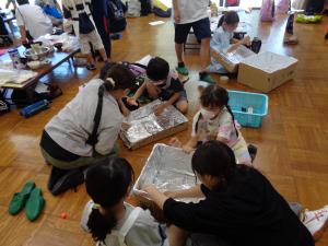 段ボールにアルミ箔を貼る作業をする子供たち