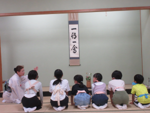 正座で整列し、講師から掛け軸の説明を受ける子どもたち