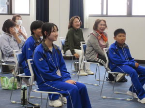 椅子に座って講師の話を聞く中学生と受講生