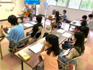 講師のギター演奏を聴く子供たちの写真