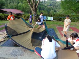 支柱を屋根から抜きテントをたたむ女子グループ