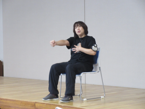 左手を胸に、右手を真っ直ぐ前に伸ばす体操の見本を見せる深澤先生