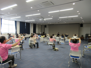 肩幅に広げた両手にタオルを持ち、体を動かす受講生の皆さん