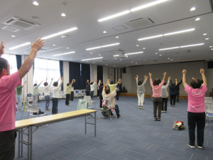 立位で両手を真上にあげ、リズムに合わせて踊る受講生の皆さん
