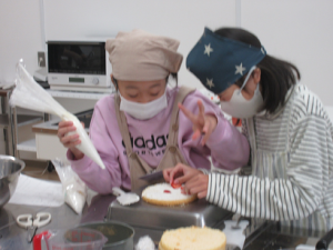 クリーム絞り袋を持つ子供、イチゴを飾り付ける子供、アイデアを出し合いながらデコレーションする様子