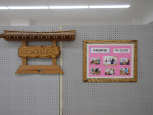 木彫りで作られた展示会場の案内板と活動の様子を紹介する写真