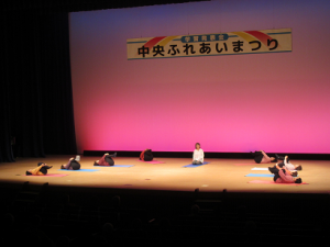 寝転んで両膝を抱えるヨガを指導される講師先生