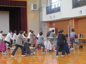 椅子の背もたれに手を置き、足の膝裏を伸ばす運動をしている様子