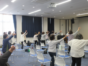 椅子から立ち上がり曲に合わせて、両手を高く突き上げている受講生の皆さん