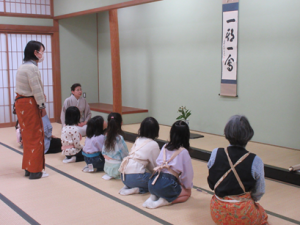 床の間の掛け軸並びにいけ花の説明を聞く受講生