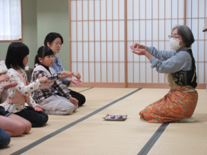 講師の手本を見ながら掌に乗せたお菓子を一口大に切り分ける受講生
