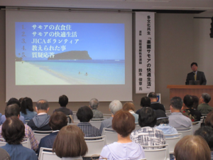 舞台左に立ち、楽園サモアについてパワーポイントのスライドを通して説明する講師