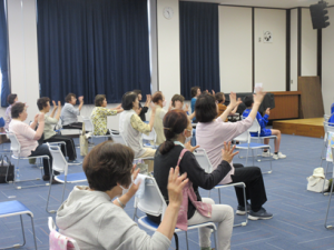 両手を前に出し脳トレを取り入れた体操をする受講生の皆さん