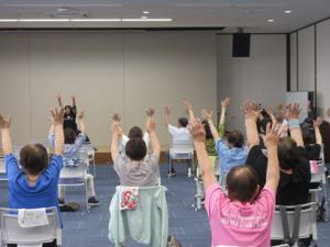講師の指導に合わせて両手を上に挙げて上半身を伸ばす受講生の皆さん