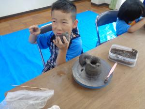 徳利とおちょこを製作中の男の子、おちょこを口にサイズの確認