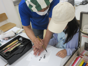 筆の持ち方を指導する講師とふるさとと平仮名で書いている受講生の子ども