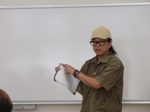 型に切断した皮を持ち縫い方の説明をする講師先生