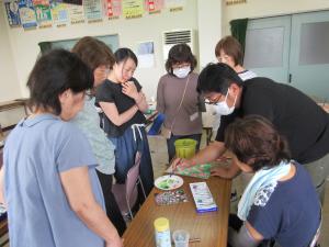 あさがおの絵に先生が絵筆で微調整されているのを受講生が机の周りに集まって見ている様子