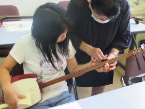 左手で弦の押さえ方を教わっている様子