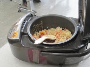 ミニトマトやサバの缶詰など数種類の具材を混ぜて炊き上がった炊飯釜の中の炊き込みご飯