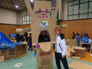 歩行型ロボットと肩を組む大学生スタッフ