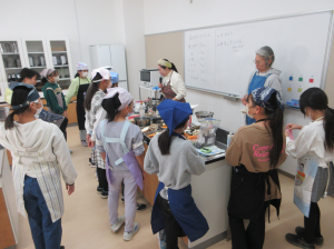 調理台の周りに集合して講師から今日のメニューを聞く受講生の子ども達