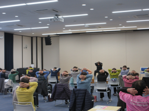 肩や背骨まわりの筋肉をほぐす運動を講師から教わり実践する受講生の皆さん