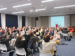 講師の指示のもと両手を挙げて楽しく脳トレに励む受講生の皆さん