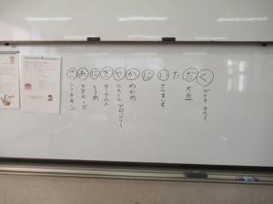 ホワイトボードに書かれた「さあにぎやかにいただく」の合言葉で本日のメニューの栄養素を学ぶ様子