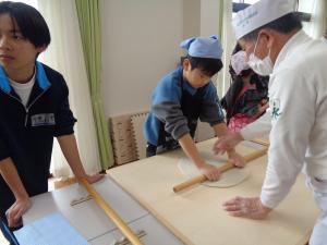 スタッフから指導を受けながら麺伸ばしに挑戦する男の子