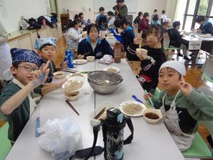 おいしそうにそばを食べながらピースをする児童たち