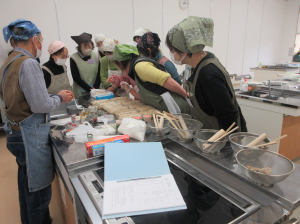 講師調理台の周りに集まり手本となる細工菓子の出来栄えの美しさにビックリしている受講生の皆さん