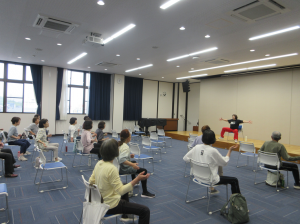 舞台中央に座り今から行うトレーニングの見本をみせる講師先生