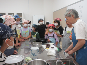 子ども達を講師調理台前に集め、揚げ物をする際の注意点を話す講師