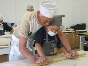 指導者と一緒にそば玉を麺棒で延ばす子ども