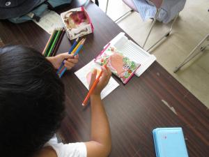 左手に色鉛筆を持って描く子供の写真