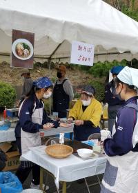 三角巾、エプロン姿で手打ちそばバザーの店員として手伝う中学生の様子